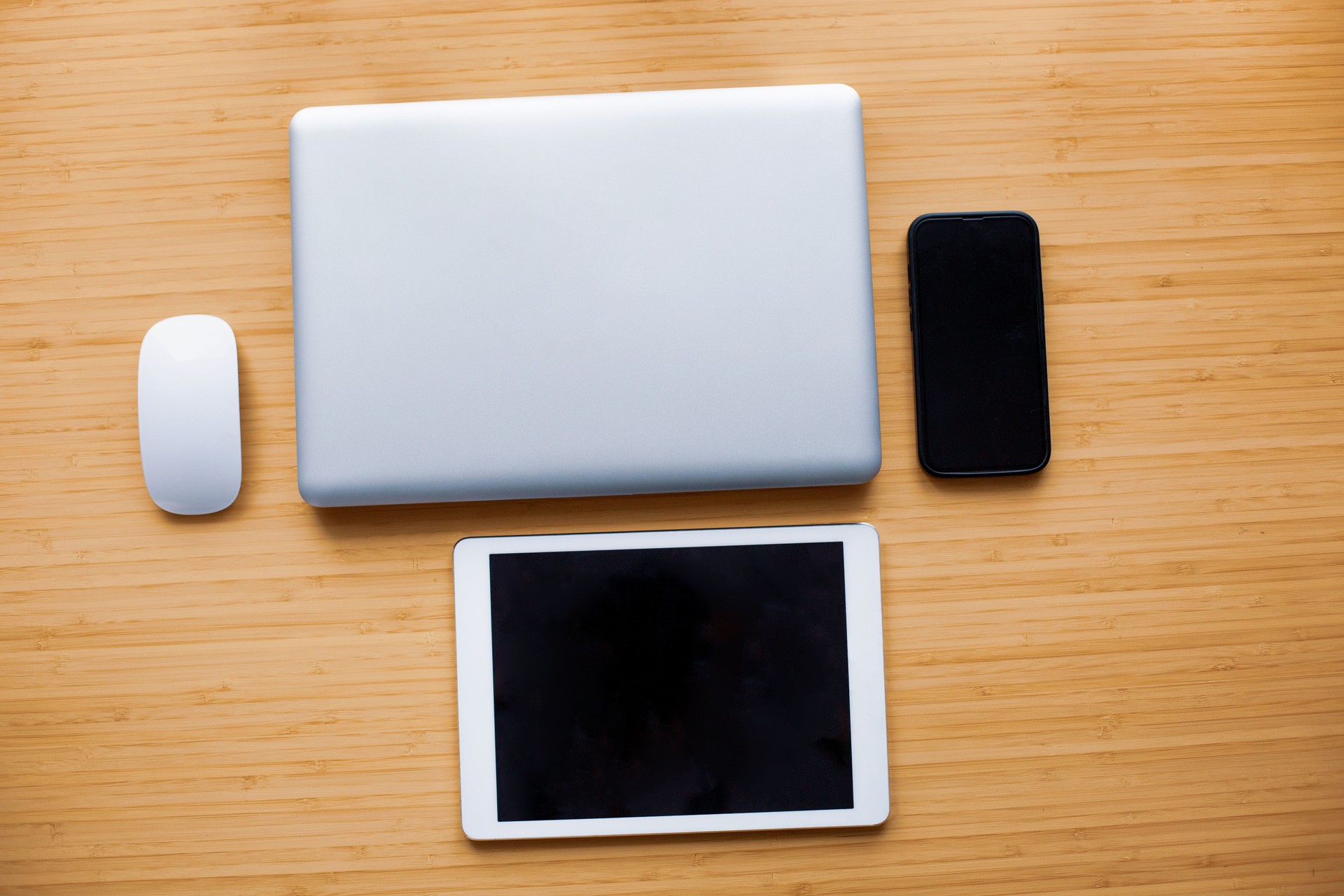 Laptop, tablet, smartphone and mouse lying on wooden desk